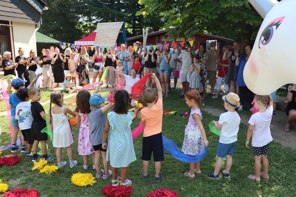 Die Kinder tanzen auf der Wiese und winken mit bunten Tüchern