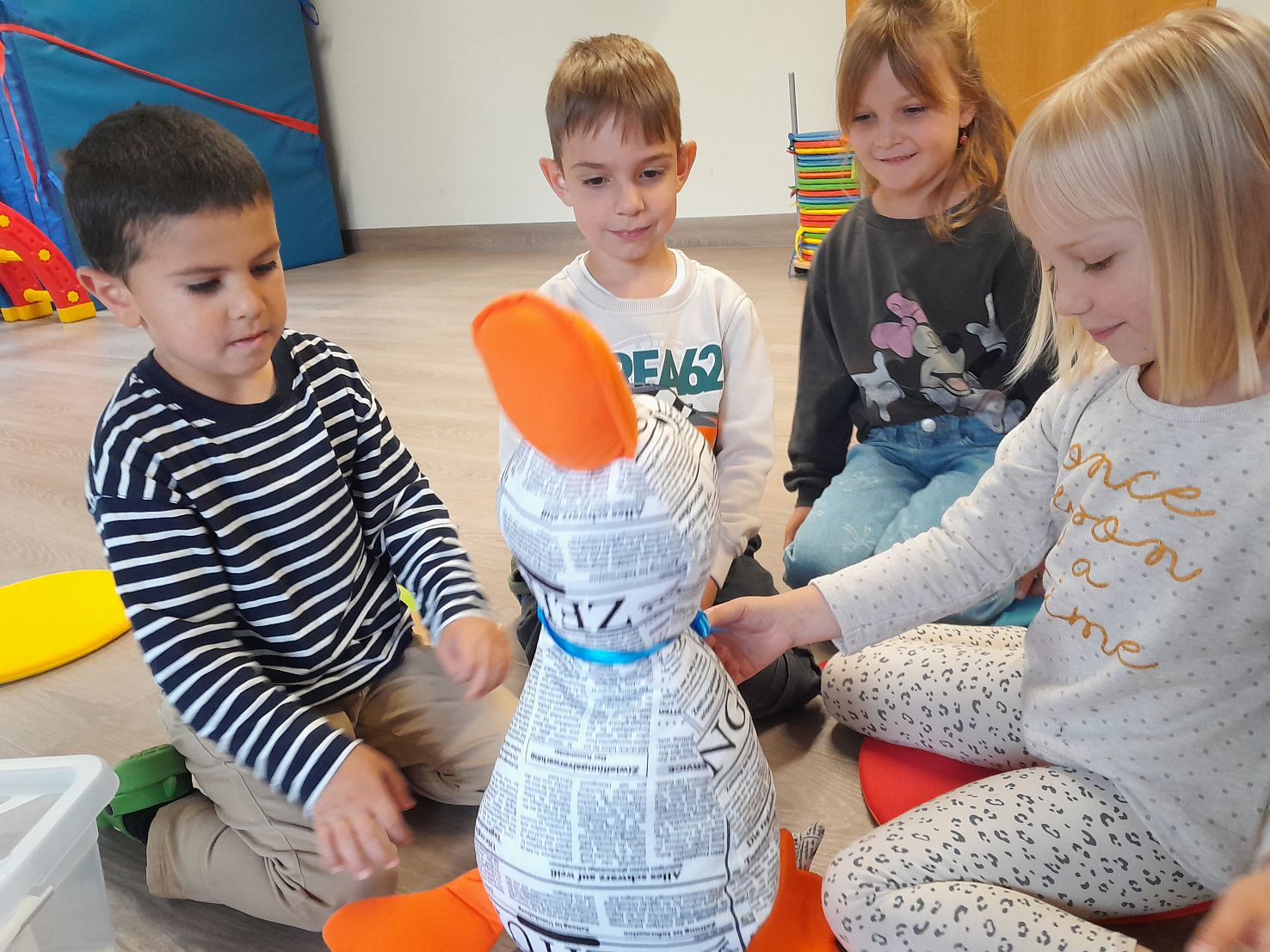 Vier Kinder sitzen im kreis um eine große weiße Stoff-Ente