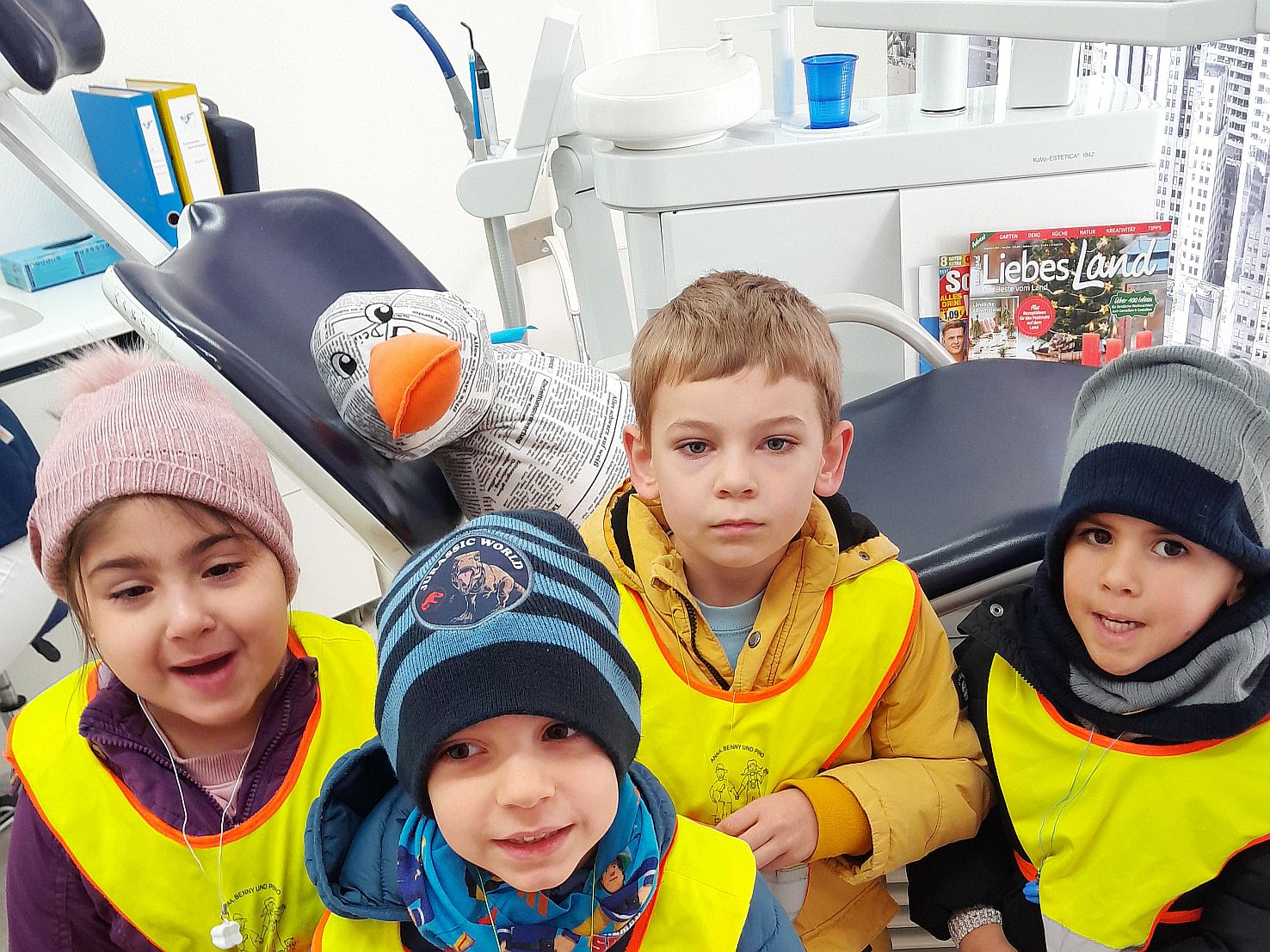 Kinder stehen vor einem Zahnarztstuhl. Auf dem liegt eine Plüschente
