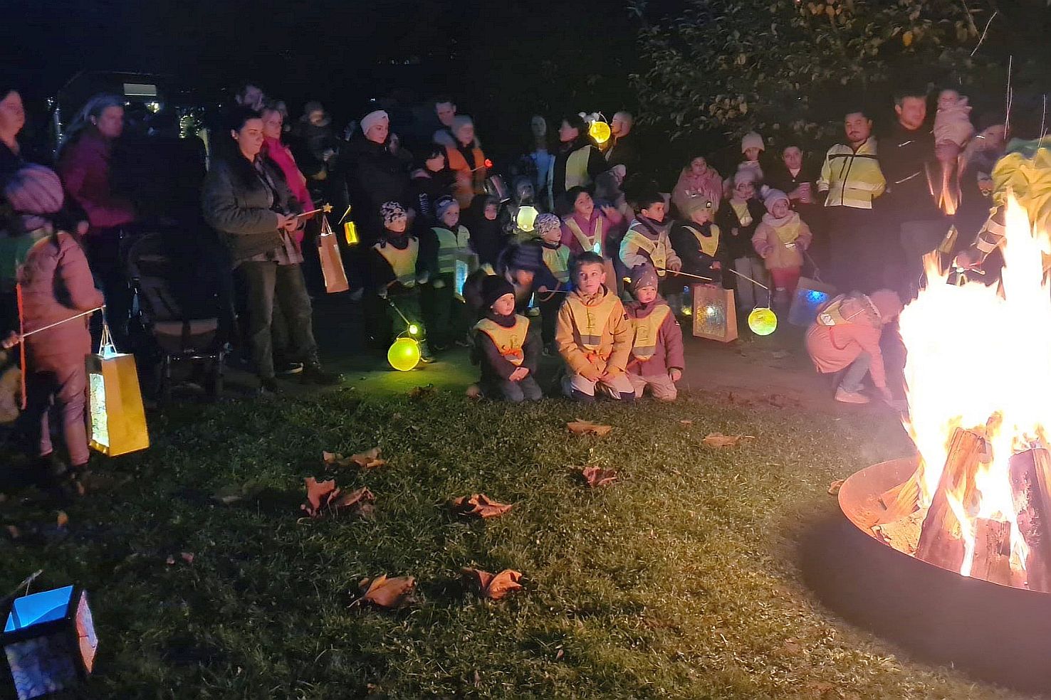 In der Dämmerung stehen Kinder mit Laternen an einem Lagerfeuer
