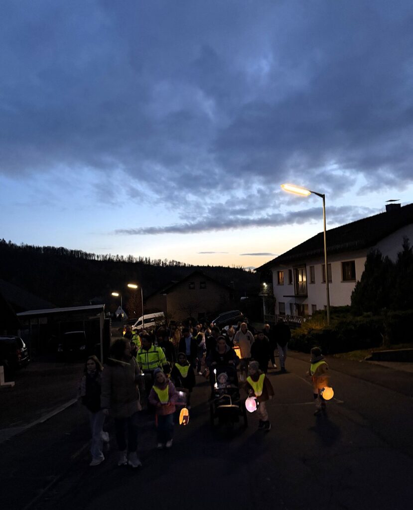 In der Dämmerung ziehen Kinder und Eltern mit Laternen eine Straße entlang