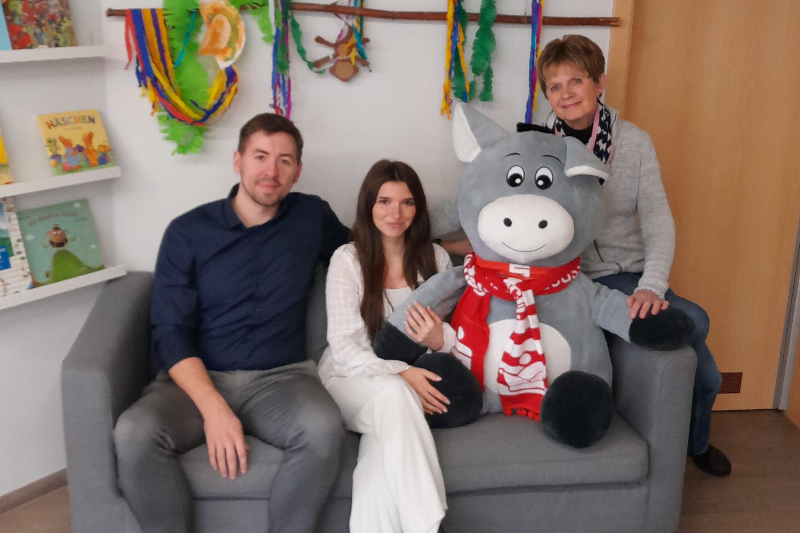 Spende KSK_Albertz 2026 3 Drei Menschen sitzen mit dem Plüschesel auf einem Sofa