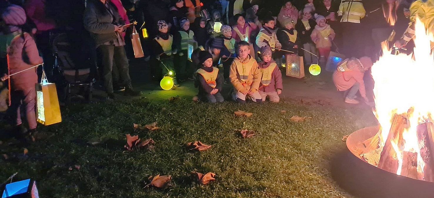 In der Dämmerung stehen Kinder mit Laternen an einem Lagerfeuer