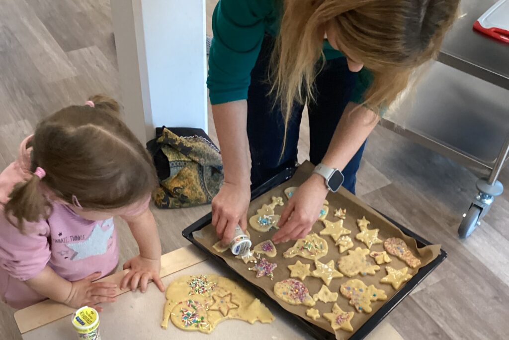 Ein Mädchen und ihre Mutter beugen sich über ein Backblech mit ausgestochenem Plätzchenteig