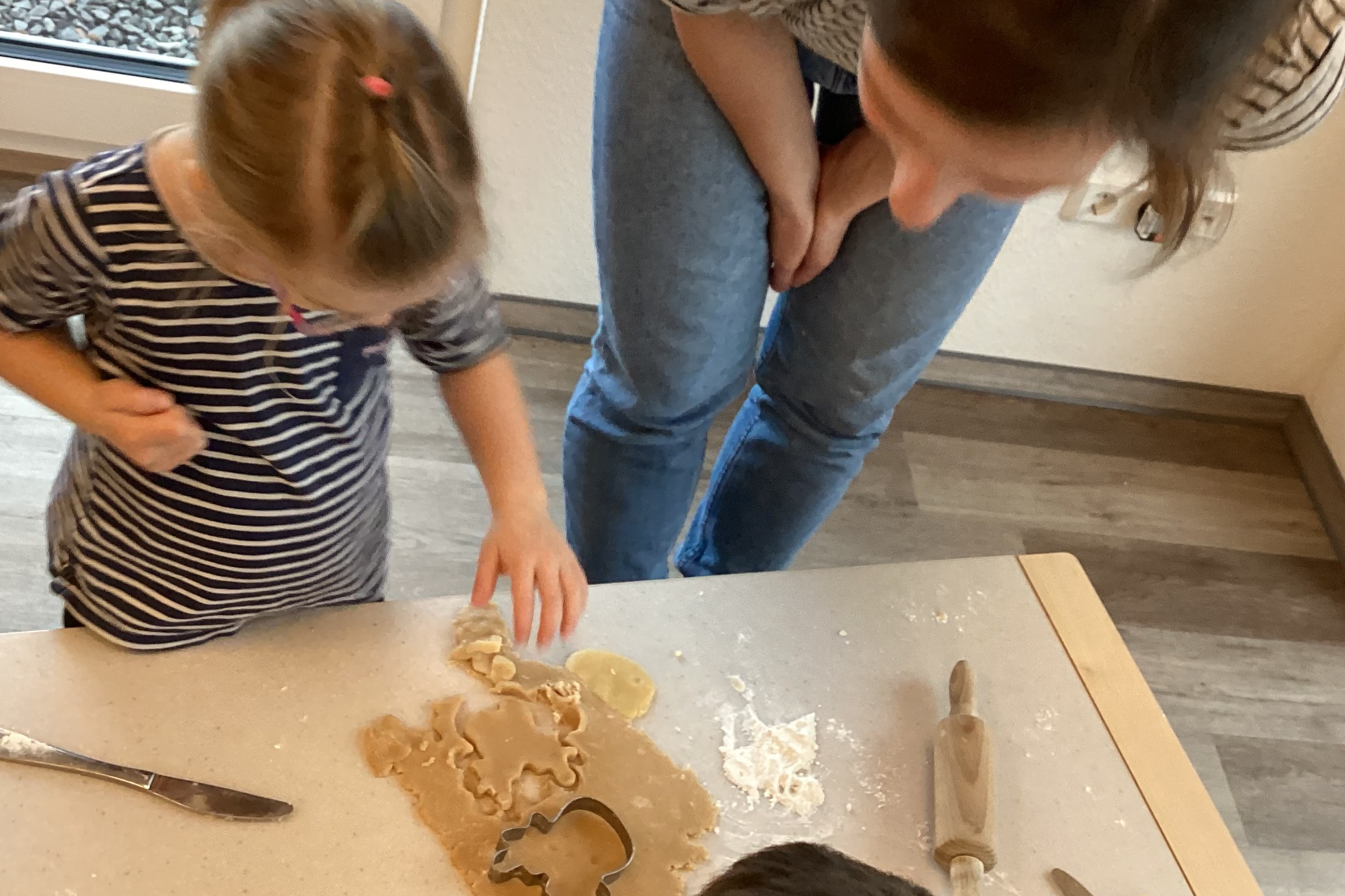 Plätzchen backen 2025 (2) Ein Mädchen und seine Mutter beugen sich über den ausgerollten Plätzchenteig