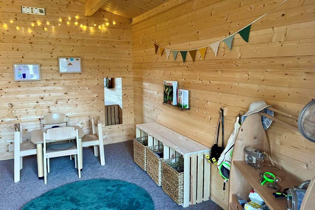 Wuselhaus_2025 4 Im Inneren des Häuschens stehen kleine Stühle um eine Tisch, ein Sideboard und Bilder hängen an der Wand.