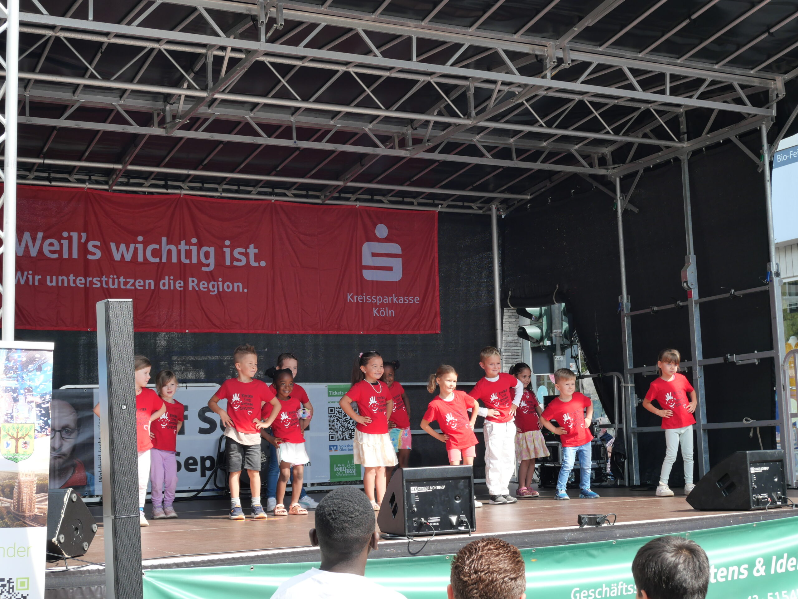 Kinder stehen bei einem Auftritt auf einer Bühne und tragen alle rote T-Shirts