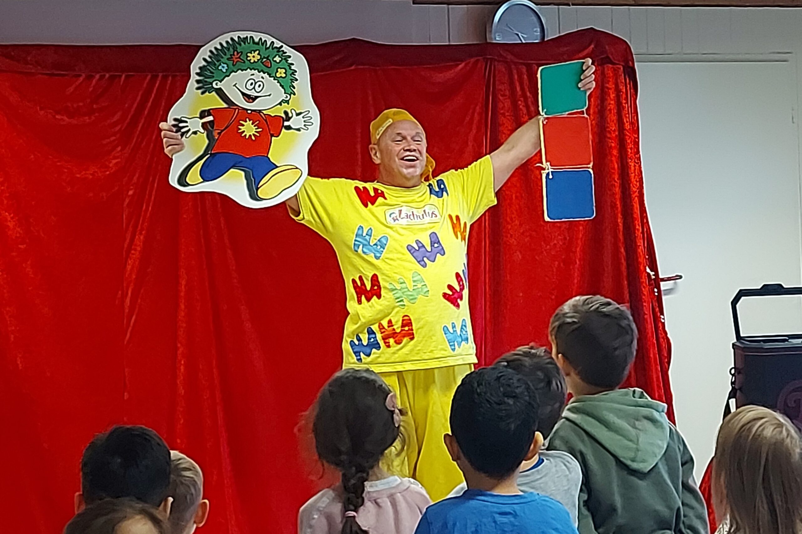 Lachulus in Waldbröl_2025 (1) EIn Mann im gelben Kostüm hält auf der Bühne lachend eine Comicfigur in die Höhe