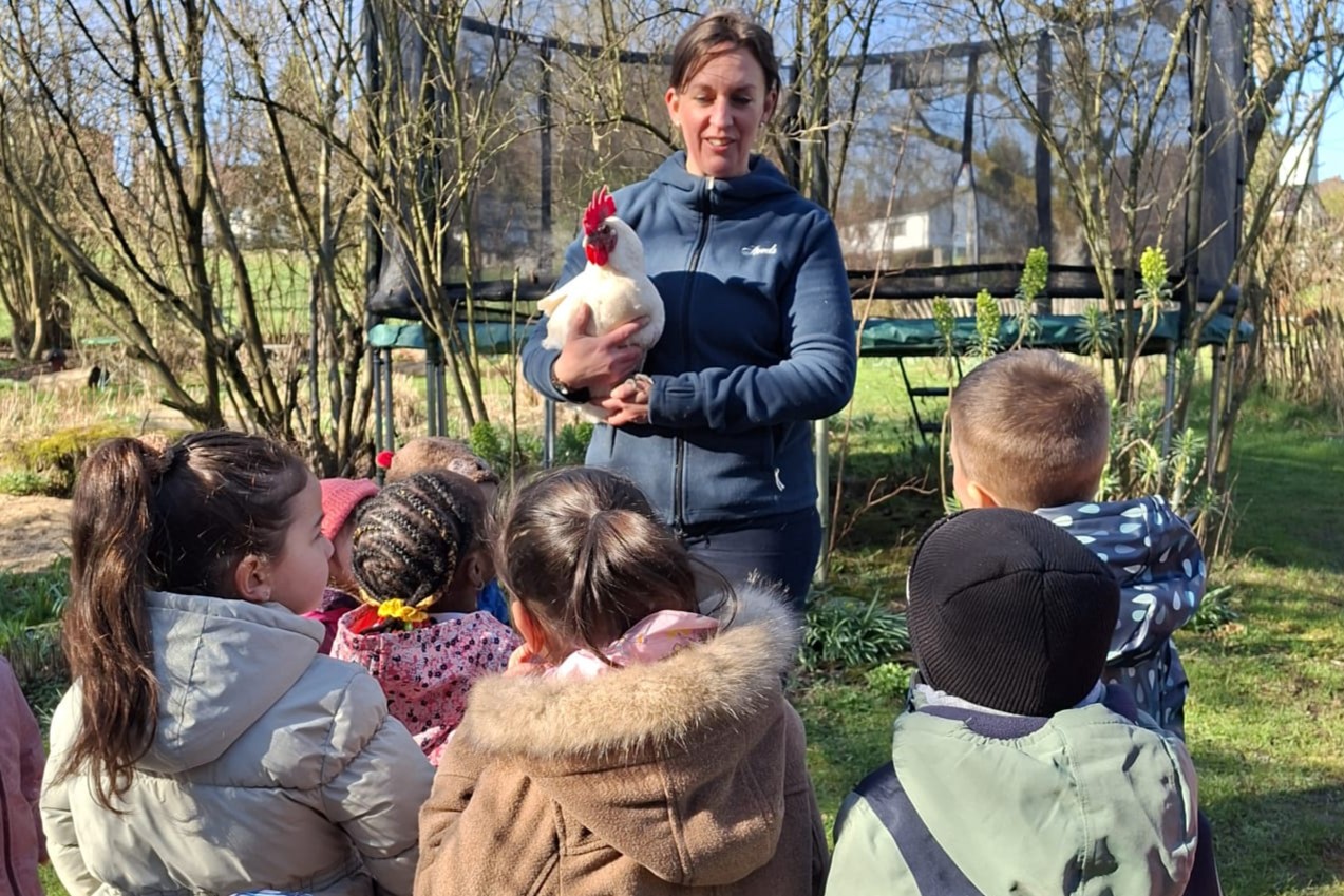 Eine junge Frau hält ein Huhn in den Armen und spricht vor einer Gruppe Kinder
