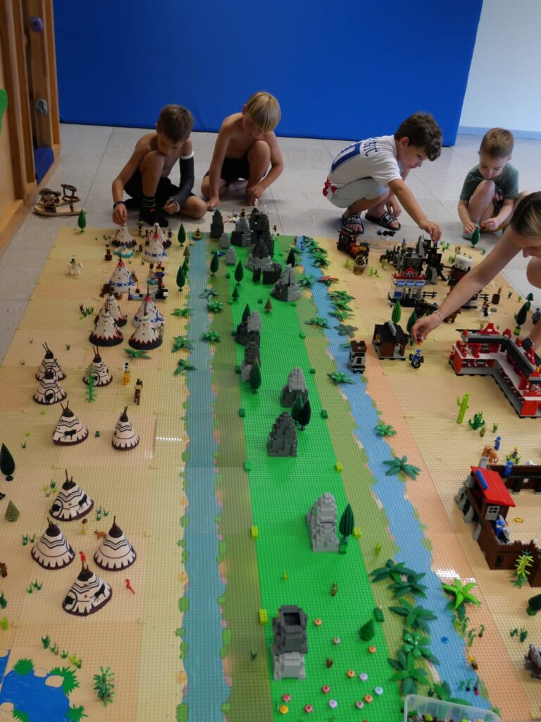 Auf dem Boden entsteht eine Westernstadt. Die Kinder hocken davor.