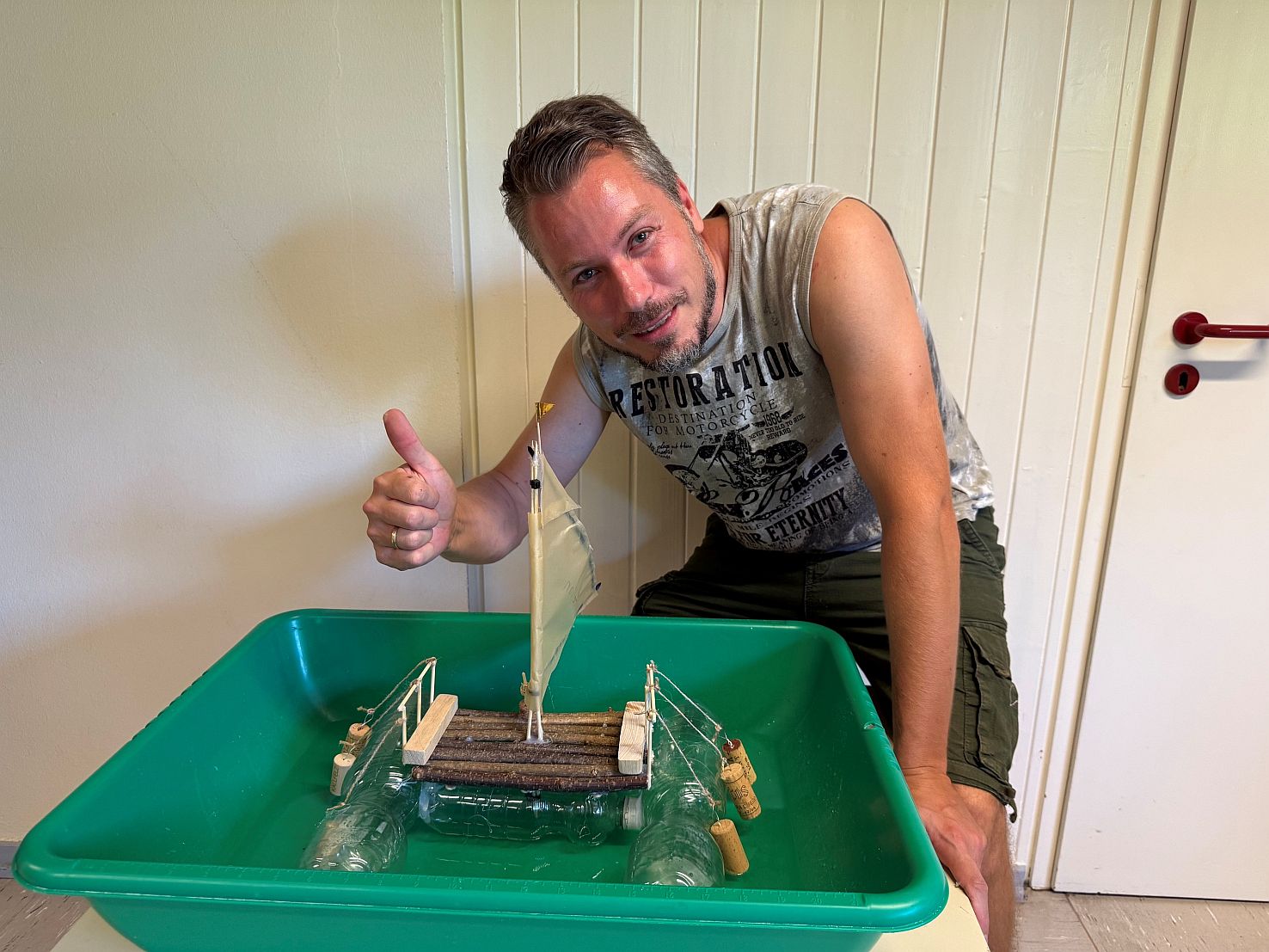 Ein Vater zeigt Daumen och vor einem selbstgebastelten Schiff auf dem Tisch