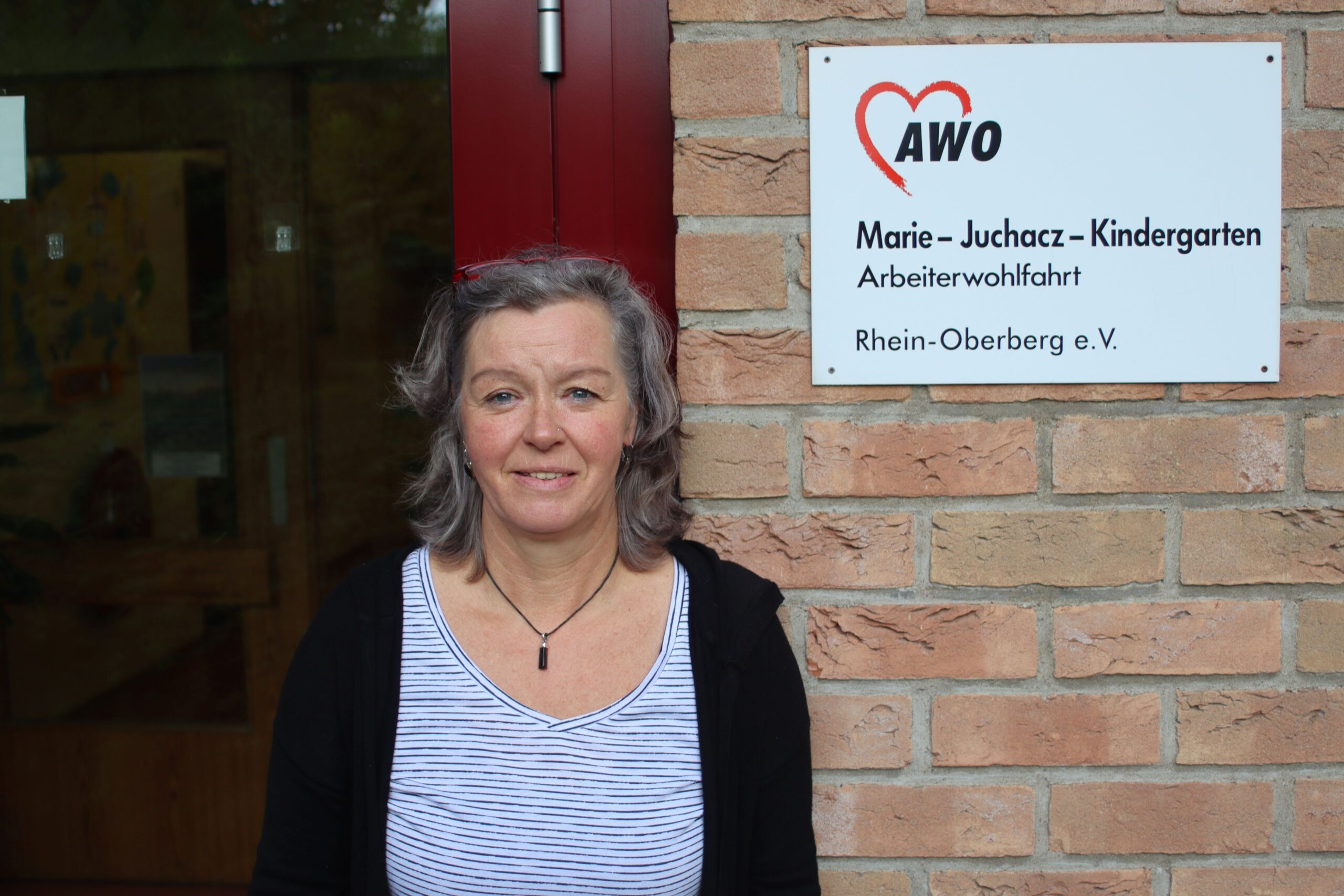 Karola Pauli Einrichtungsleitung vor dem Schild der KiTa, auf dem der Name der Einrichtung steht