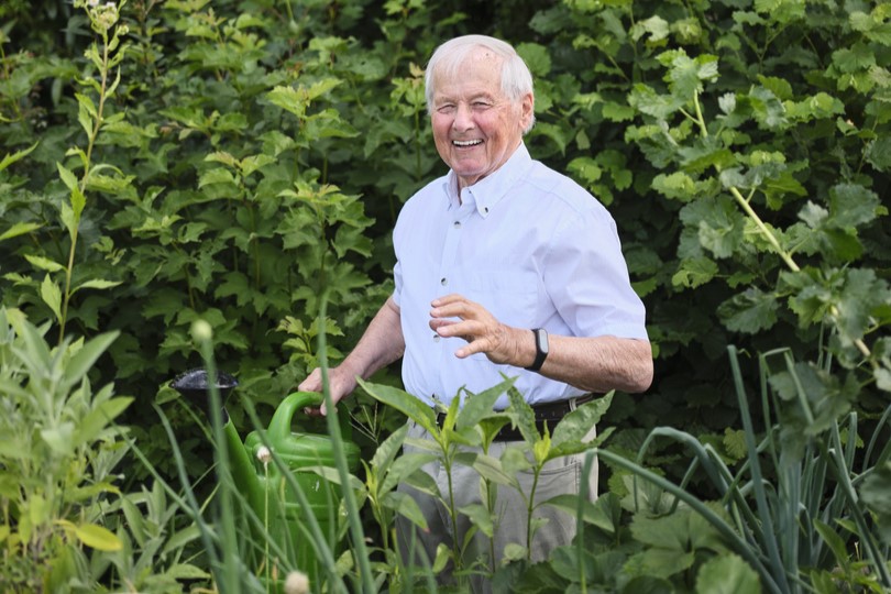 Symbolbild: Ein älterer Herr steht lachend im Garten. Er hält eine Gießkanne in der Hand.