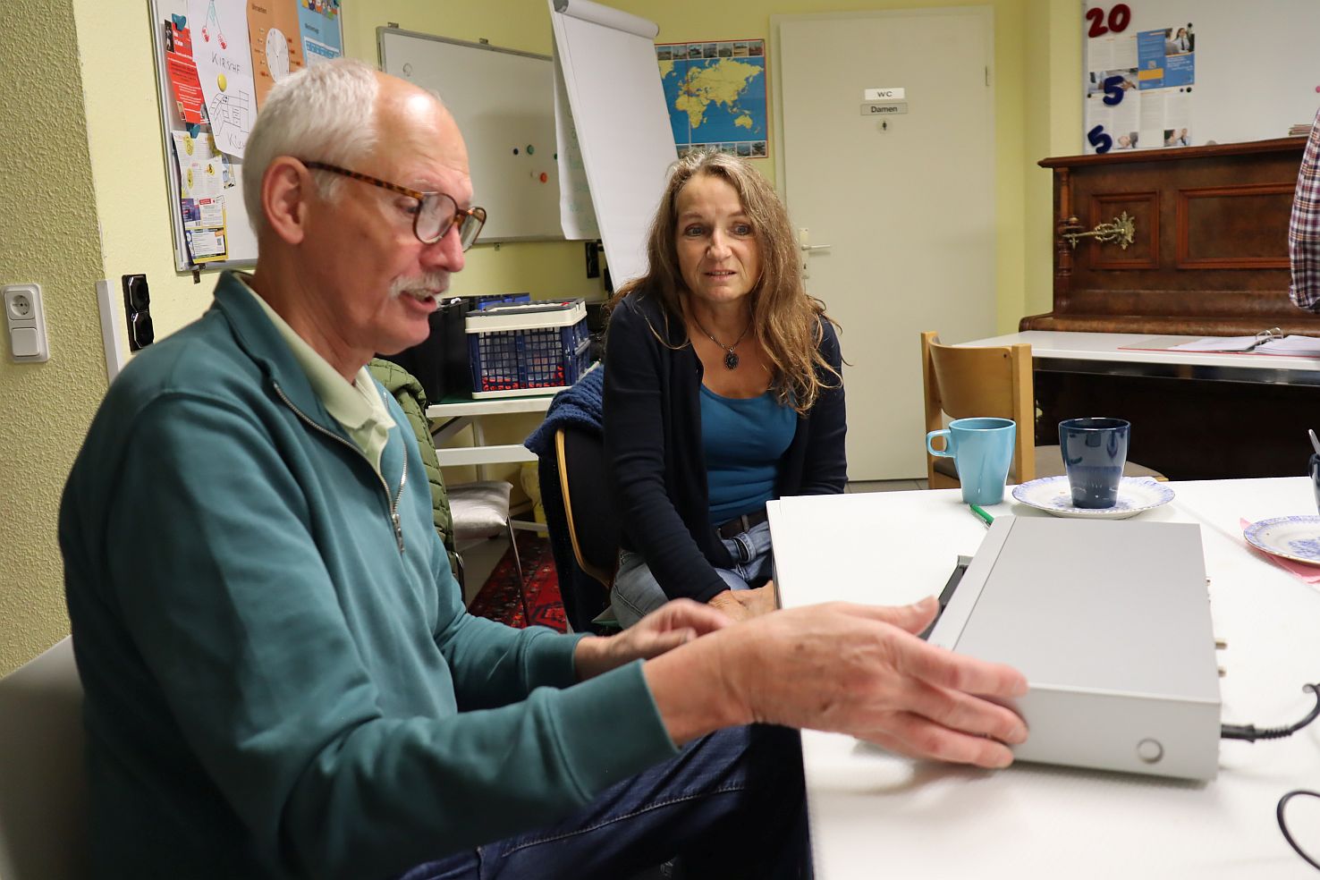 Ein Mann und eine Frau schauen sich am Tisch einen DVD-Spieler an